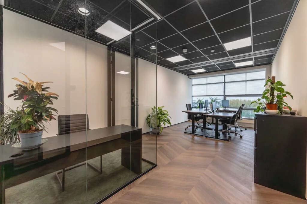 Modern kantoorinterieur aan de Joop Geesinkweg met glazen vergaderruimte, bureaus en groene kamerplanten.